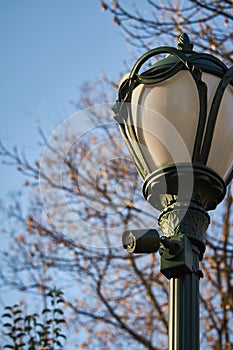 Vintage lantern with a surveillance camera in a public park in autumn in front of a blue sky, selective focus