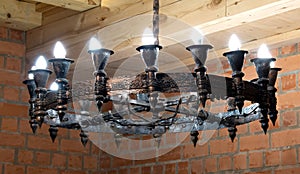 Vintage large vintage chandelier with candle light bulbs hanging from a wooden ceiling. Metal openwork frame with forged ornament