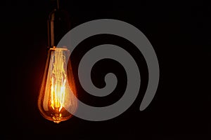 Vintage light bulb on black background, copy space. Glowing edison bulb