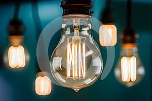 Vintage light bulb with visible filament strands suspended, emitting warm yellow light against teal background