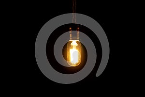 Vintage lightbulb hanging on black background. Incandescent lamp isolated on a black