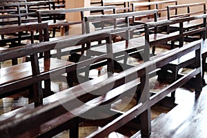 Vintage long wooden chairs for sitting and praying for blessings in Christian churches. Rows of church benches in sunlight