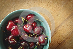 Vintage looking image of a light blue bowl full of red cherries on a wooden board.