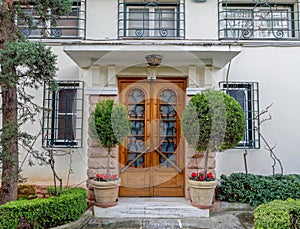 A vintage luxury house facade with ornate natural wooden door, garden and potted flowers.
