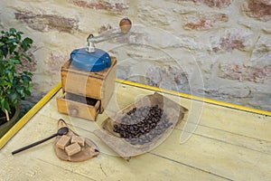 Vintage manual coffee grinder and coffee beans on old wooden table. Background - stone wall