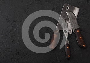 Vintage meat knife and fork and hatchet on black table background. Butcher utensils. Space for text