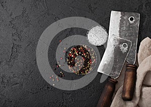 Vintage meat knife hatchets on black stone table background. Butcher utensils. Salt and pepper. Space for text