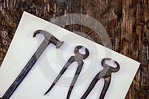 Vintage metal hand tool. Tongs and a hammer and nailer on a dirty sheet of paper. Cobbler`s or carpenter`s craft. Wooden