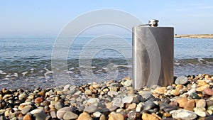 Vintage metal hip flask on pebbles on a beach.