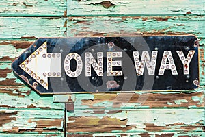 Vintage metal One Way road sign on weathered green wooden door locked with rusty padlock