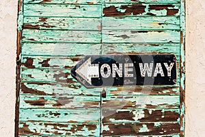 Vintage metal One Way road sign on weathered green wooden door locked with rusty padlock