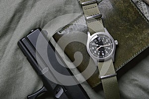 Vintage military watch with nato strap and pistol on army green background, Classic timepiece mechanical wristwatch