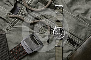 Vintage military watch with nato strap and tactical belt on army green background, Classic timepiece mechanical wristwatch