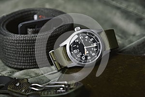 Vintage military watch and tactical belt on army green background, Classic timepiece mechanical wristwatch photo