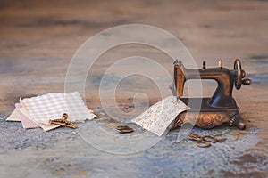 Vintage mini sewing machine with scissors, buttons and fabric on rustic background