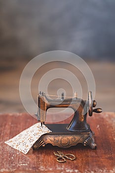 Vintage mini sewing machine with scissors, buttons and fabric on rustic background