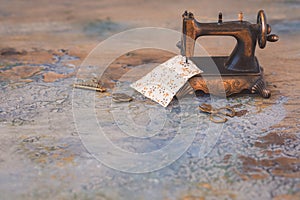 Vintage mini sewing machine with scissors, buttons and fabric on rustic background