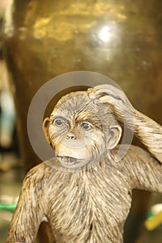 Vintage monkey statuette with hand on head in front of a brass vase in browns and golds