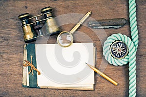 Vintage notebook, compass, binoculars, old pocket knife, pencil, magnifying glass on wooden desk background
