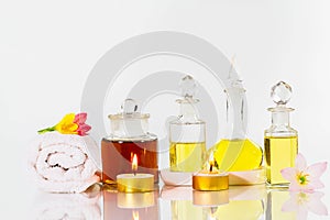 Vintage old bottles of aromatic oils with candles, flowers and white towel on glossy white table on white background