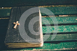 Vintage old holy bible book, grunge textured cover with wooden christian cross. Retro styled image on wood background.