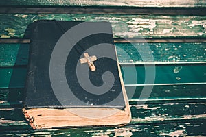 Vintage old holy bible book, grunge textured cover with wooden christian cross. Retro styled image on wood background.