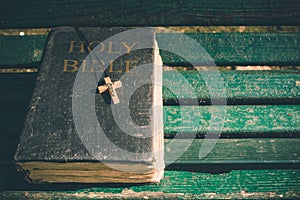 Vintage old holy bible book, grunge textured cover with wooden christian cross. Retro styled image on wood background.