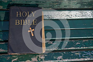 Vintage old holy bible book, grunge textured cover with wooden christian cross. Retro styled image on wood background.