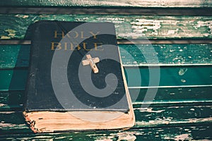 Vintage old holy bible book, grunge textured cover with wooden christian cross. Retro styled image on wood background.