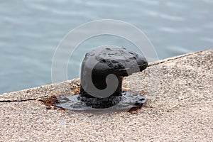Vintage old restored and freshly and painted black old iron mooring bollard screwed on local concrete pier with four metal bolts