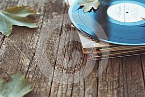 Vintage old vinyl records on wooden autumn background, selective focus decorated with few leaves. Music, fashion, texture,