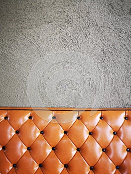 Vintage orange or brick colour leather sofa with grey concrete wall background.