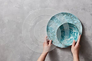 Vintage painted glazed plates dishes on gray concrete table with free space ror text. Girl hold handcraft bowl in her