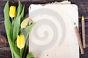 Vintage paper, pencils and yellow tulips on wooden background. Free space for your text.