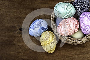 Vintage pastel color easter eggs in a wicker basket on a dark wooden background.