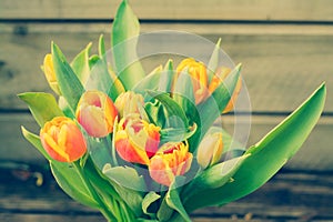 Vintage photo of beautiful orange tulips on a rustic wooden background.