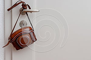 Vintage photo camera hanging on door handle white wall.