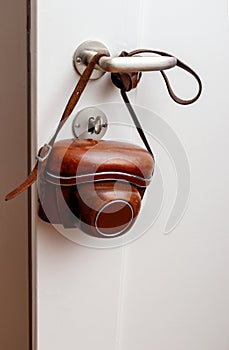 Vintage photo camera hanging on door handle white wall.