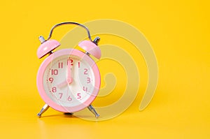 Vintage pink alarm clock on yellow background.