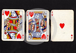 Vintage playing cards showing a run of queen, king and ace of hearts on a black background.