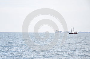 Vintage pleasure boat sailing in the Mediterranean Sea near Barcelona. Cargo ships and tankers on the background