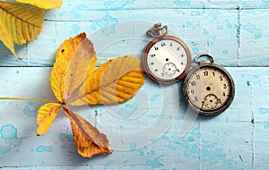 vintage pocket clock and autumn leaves on a blue painted wood suraface