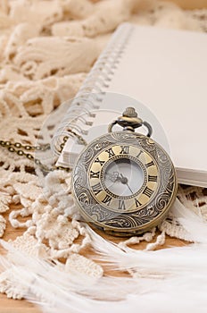 Vintage pocket watch with blank note book on lace background