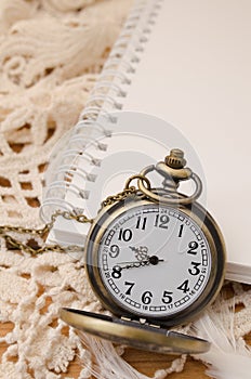 Vintage pocket watch with blank note book on lace background