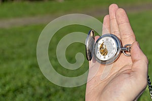 Vintage pocket watch in male hand on a background of green grass. Steampunk watch. Sunny summer day. The clock mechanism is