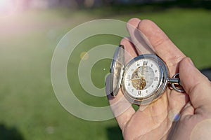 Vintage pocket watch in male hand on a background of green grass. Steampunk watch. Sunny summer day. The clock mechanism is