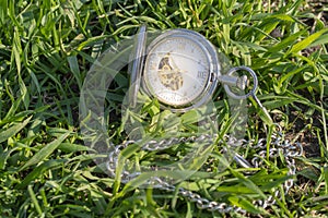 Vintage pocket watch in male hand on a background of green grass. Steampunk watch. Sunny summer day. The clock mechanism is