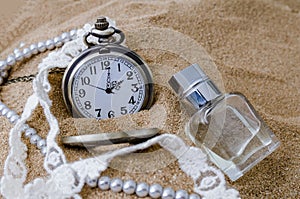 Vintage pocket watch with perfume on sand background