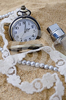 Vintage pocket watch with perfume on sand background