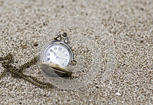 Vintage pocket watch is on the sand.